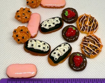 May include: Miniature food assortment including cookies, eclairs, and tarts. The cookies are orange with dark brown spots. The eclairs have white and black frosting. The tarts have a strawberry or chocolate drizzle. A purple ruler shows the size in inches.