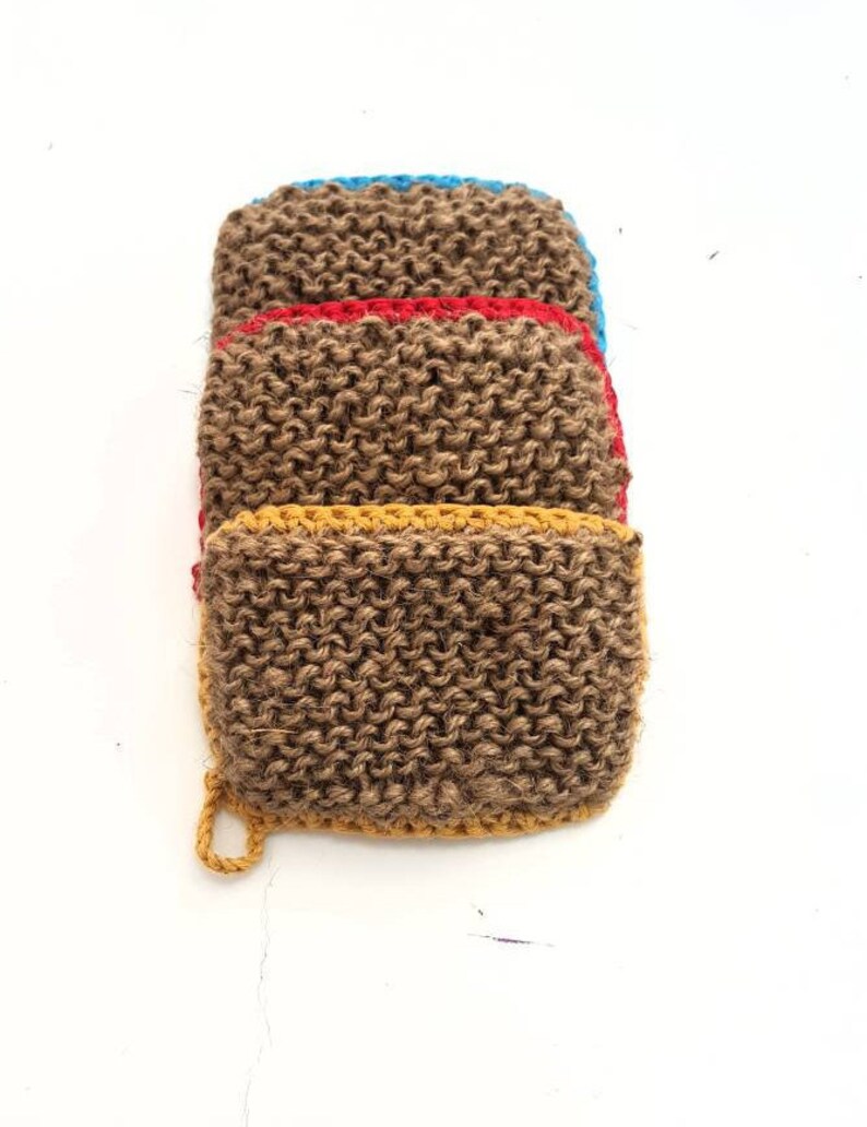 May include: A stack of four brown knitted dishcloths with colourful trim. The top dishcloth has a blue trim, the next has a red trim, the next has a yellow trim, and the bottom dishcloth has a yellow trim.