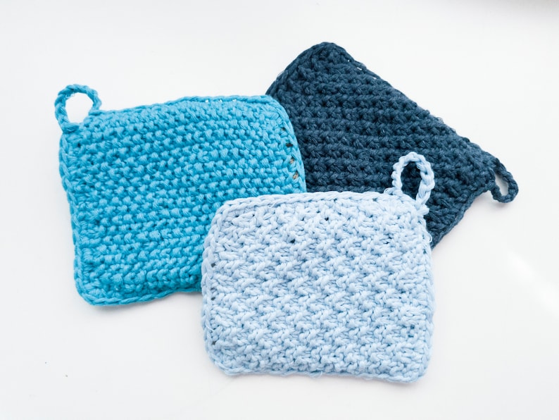 May include: Three crocheted pot holders in blue, light blue, and dark blue. Each pot holder has a loop handle.