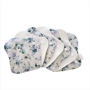 May include: A set of six reusable cloth menstrual pads with a floral print in shades of green and purple. The pads have a white cotton backing and are labeled "Friend".