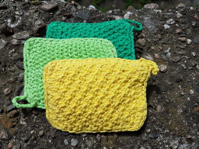 May include: Three crocheted dishcloths in green, light green, and yellow. The dishcloths are stacked on top of each other.