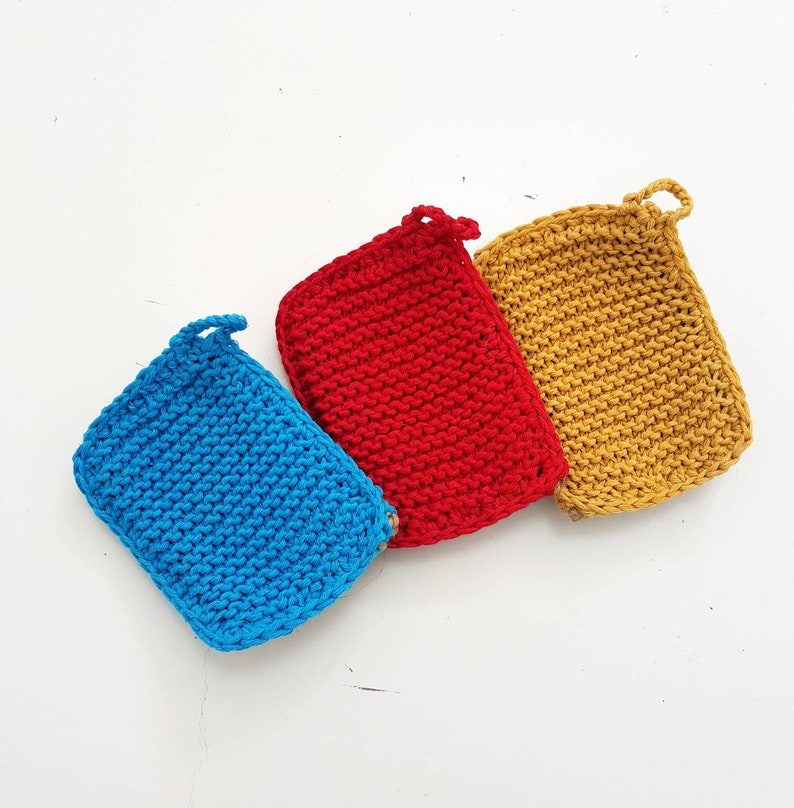 May include: Three knitted dishcloths in blue, red and yellow. Each dishcloth has a loop handle.