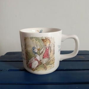 May include: White ceramic mug with a charming illustration of a fox and a goose in a woodland scene. The mug has a curved handle and the text "Qu" is visible. A delightful item for any kitchen or a lovely gift.