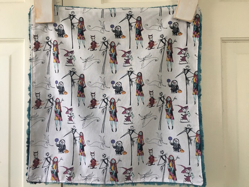 May include: A white fabric with a teal border features a repeating pattern of Jack Skellington and Sally from The Nightmare Before Christmas. The characters are depicted in various poses, including holding pumpkins and sweets.
