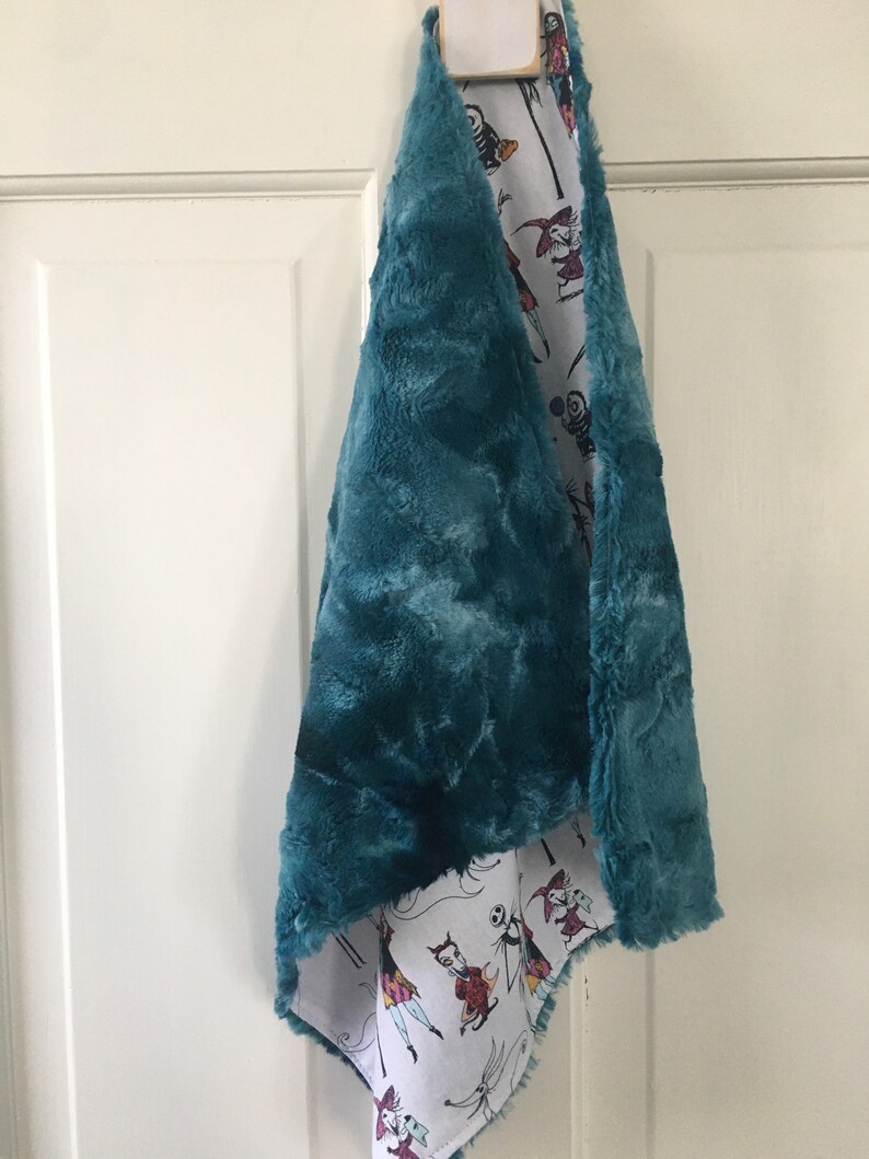 May include: Teal faux fur scarf with a white cotton lining featuring a repeating pattern of characters from The Nightmare Before Christmas.