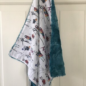 May include: A white and teal baby blanket featuring a Nightmare Before Christmas print. The blanket depicts various characters from the film, including Jack Skellington, Sally, and Oogie Boogie.