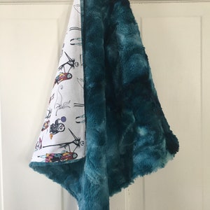 May include: A teal plush baby blanket with a white cotton side featuring a Nightmare Before Christmas print. The blanket is folded and hanging on a white door.