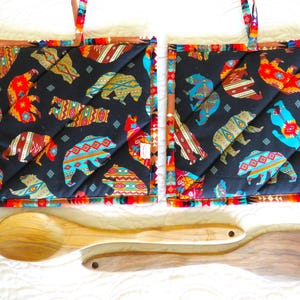 Peut inclure: Deux maniques de cuisine matelassées noires avec un motif géométrique coloré représentant des ours, une cuillère en bois et une spatule.