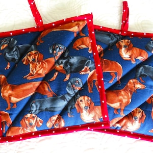 May include: Two red and white polka dot oven mitts with a blue background and a pattern of dachshund dogs.