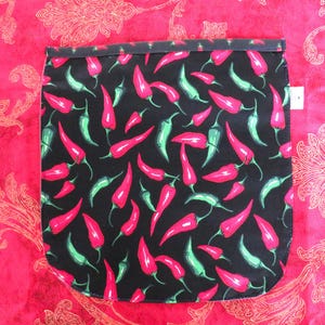 May include: A rectangular fabric pouch featuring a black background with a repeating pattern of red and green chili peppers. The pouch has a dark top border and a small white tag on the right side, showcasing a vibrant culinary-themed design.