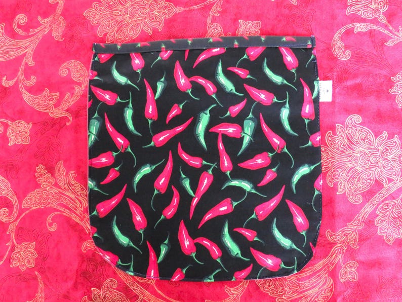 May include: A rectangular fabric pouch featuring a black background with a repeating pattern of red and green chili peppers. The pouch has a dark top border and a small white tag on the right side, showcasing a vibrant culinary-themed design.
