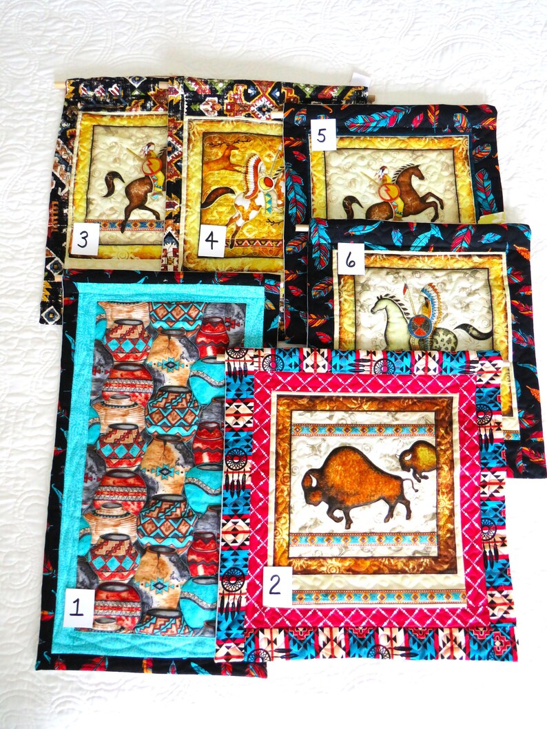May include: A collection of six small, quilted wall hangings with Native American themes. The hangings feature images of pottery, bison, and Native Americans on horseback. Each piece has a decorative border in various colors and patterns.