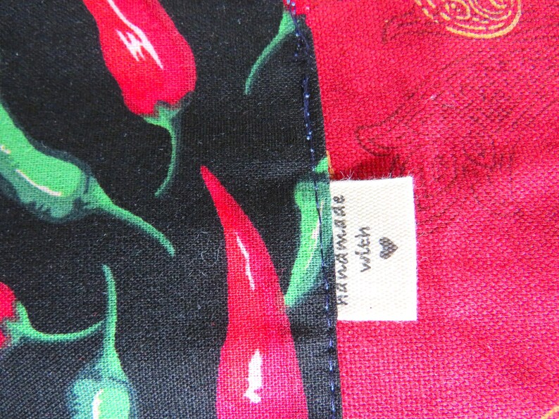 May include: A fabric item featuring a black section with a pattern of red and green chili peppers and a solid red section. A small white rectangular tag is sewn into the seam, displaying the text "handmade with" followed by a heart symbol.