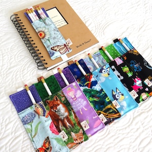Peut inclure: Plusieurs étuis à crayons aux motifs variés, notamment floraux, renards et personnages de dessins animés. Chaque étui contient un crayon et est présenté avec un carnet à spirales. Les étuis sont en tissu et de couleurs variées.