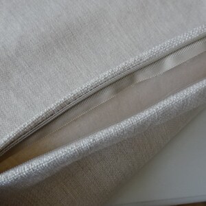 May include: A close-up of a beige pillow with a zipper closure. The pillow is made of a soft, textured fabric.