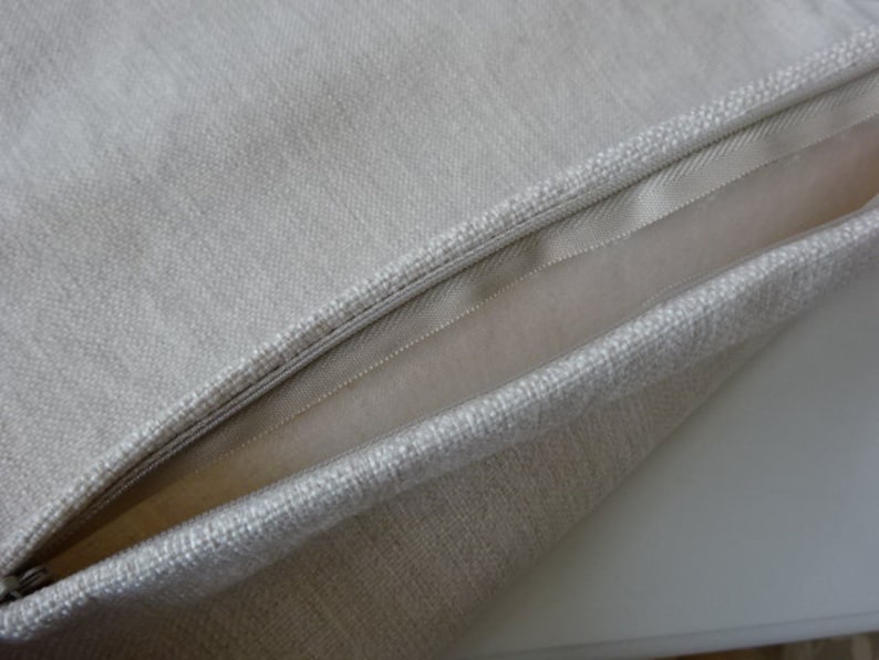 May include: A close-up of a beige pillow with a zipper closure. The pillow is made of a soft, textured fabric.