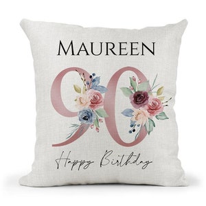 May include: A white cushion with the name "MAUREEN" and the number "90" in pink with floral accents. The text "Happy Birthday" is written below the number.