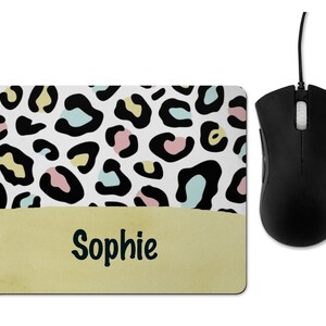 May include: A white mouse mat with a black and white leopard print pattern with pastel blue, pink, and yellow accents. The bottom portion of the mouse mat is a solid yellow colour with the name "Sophie" written in black.