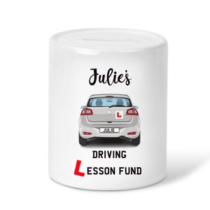 May include: White ceramic money box with a cartoon illustration of a silver car with a red "L" on the back. The text "Julie's Driving Lesson Fund" is printed on the front of the box.