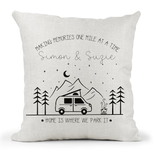 May include: A white throw pillow with black text and a graphic of a camper van in front of mountains. The text reads "Making memories one mile at a time Simon & Suzie" and "Home is where we park it."
