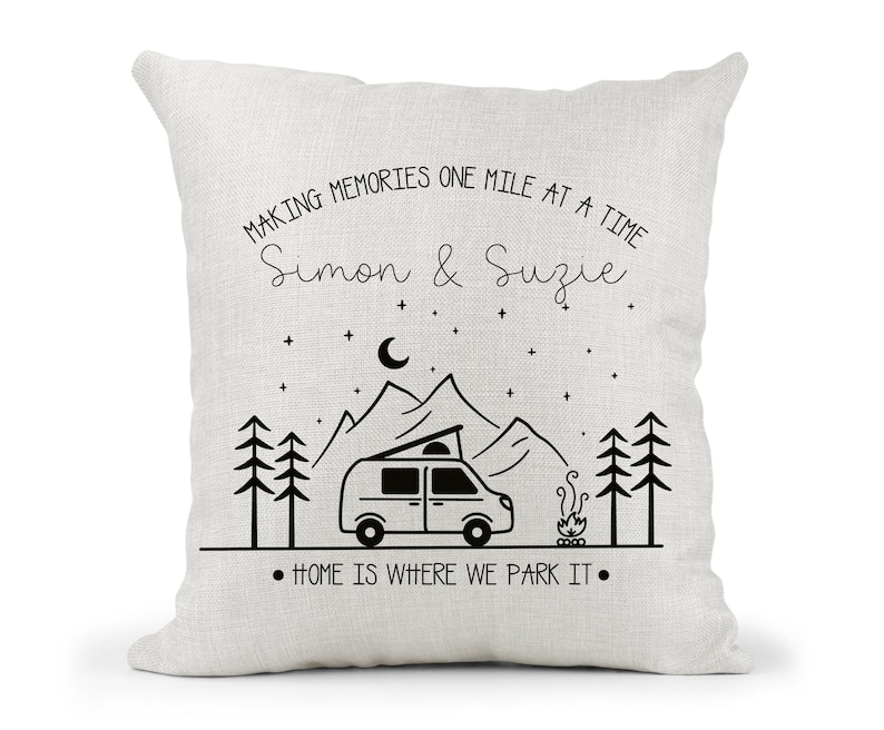 May include: A white throw pillow with black text and a graphic of a camper van in front of mountains. The text reads "Making memories one mile at a time Simon & Suzie" and "Home is where we park it."