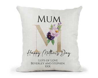 May include: A white pillow with the word "MUM" in black text and a gold letter "M" decorated with purple and pink flowers. The text "Happy Mother's Day" is written in black cursive script. The text "Lots of Love, Beverley and Stephen, XXX" is written in black text.