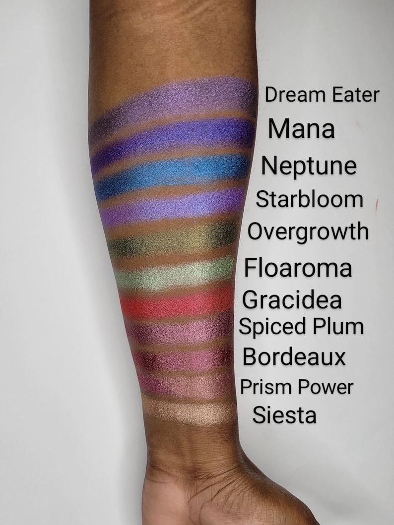 Puede incluir: Un primer plano de un brazo con 12 muestras de sombra de ojos diferentes. Las muestras est&aacute;n etiquetadas de arriba a abajo: Dream Eater, Mana, Neptune, Starbloom, Overgrowth, Floaroma, Gracidea, Spiced Plum, Bordeaux, Prism Power, Siesta.