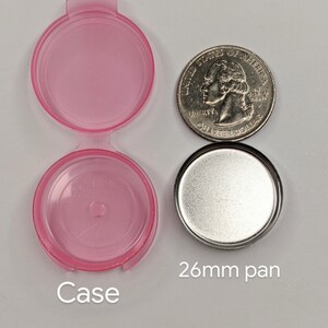 Puede incluir: Una caja de pl&aacute;stico rosa con tapa y una sart&eacute;n de metal plateado. La sart&eacute;n tiene 26 mm de di&aacute;metro. La caja es ligeramente m&aacute;s grande que una moneda de 25 centavos de d&oacute;lar estadounidense.