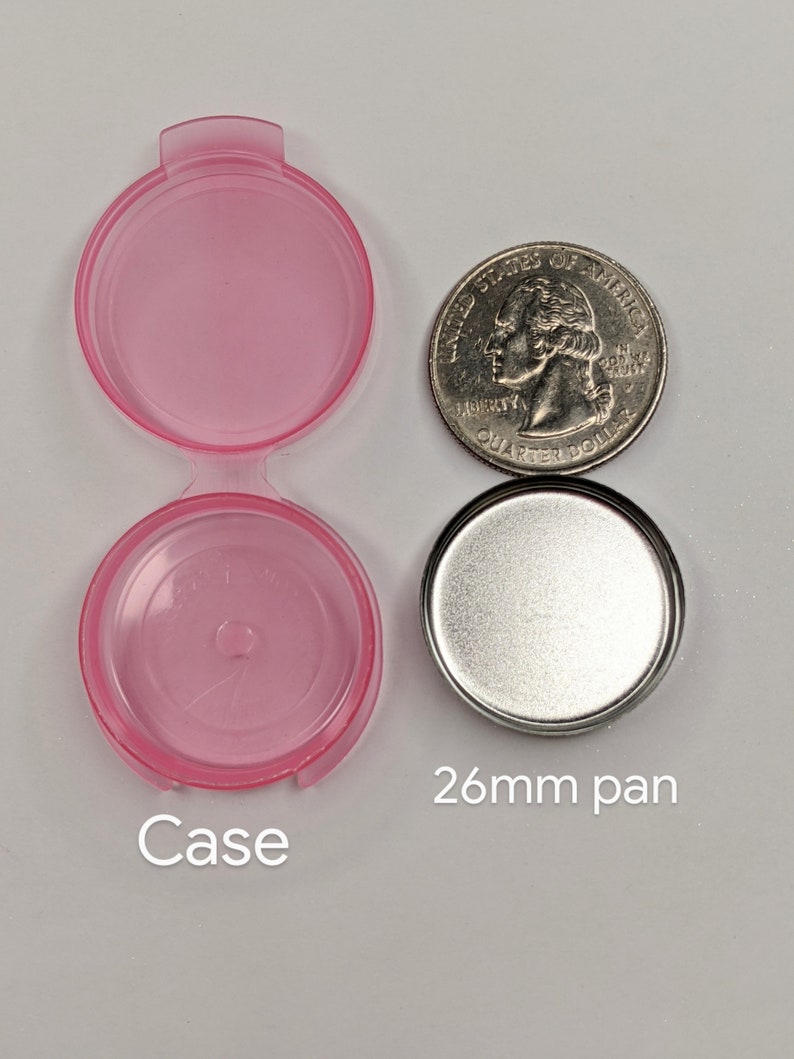 Puede incluir: Una caja de pl&aacute;stico rosa con tapa y una sart&eacute;n de metal plateado. La sart&eacute;n tiene 26 mm de di&aacute;metro. La caja es ligeramente m&aacute;s grande que una moneda de 25 centavos de d&oacute;lar estadounidense.