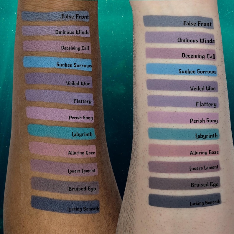 May include: Two arms display eyeshadow swatches in various shades of purple, blue, and pink. Each swatch is labeled with a name, such as "False Front" and "Ominous Winds." The background is a teal color with white specks.