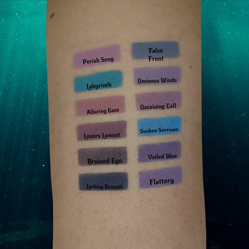 May include: A collection of eyeshadow swatches in various shades of purple, blue, and pink. Each swatch has a unique name printed below it, such as "Perish Song" and "Labyrinth". The swatches are displayed on a person's arm.