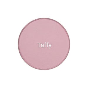 Puede incluir: Un compacto de sombra de ojos redondo de color rosa con la palabra "Taffy" impresa en blanco en la superficie.