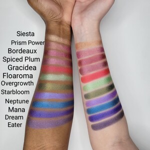 Puede incluir: Primer plano de dos brazos con muestras de sombra de ojos. Las muestras est&aacute;n etiquetadas con nombres como "Siesta", "Prism Power", "Bordeaux", "Spiced Plum", "Gracidea", "Floaroma", "Overgrowth", "Starbloom", "Neptune", "Mana", "Dream" y "Eater".