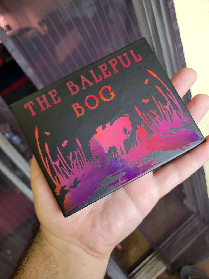 Op de afbeelding: Een zwarte doos met een holografische afbeelding van een paard in een moeras. De doos heeft de tekst "The Baleful Bog" op de voorkant.