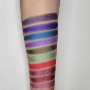 Puede incluir: Un primer plano de un brazo con muestras de sombra de ojos en varios colores, incluyendo morado, azul, verde, rojo y marr&oacute;n.