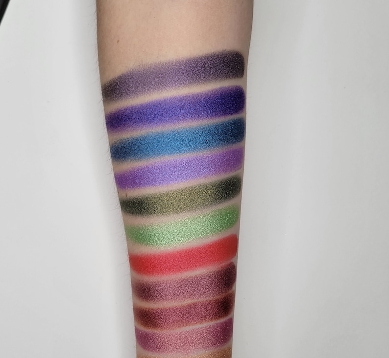 Puede incluir: Un primer plano de un brazo con muestras de sombra de ojos en varios colores, incluyendo morado, azul, verde, rojo y marr&oacute;n.
