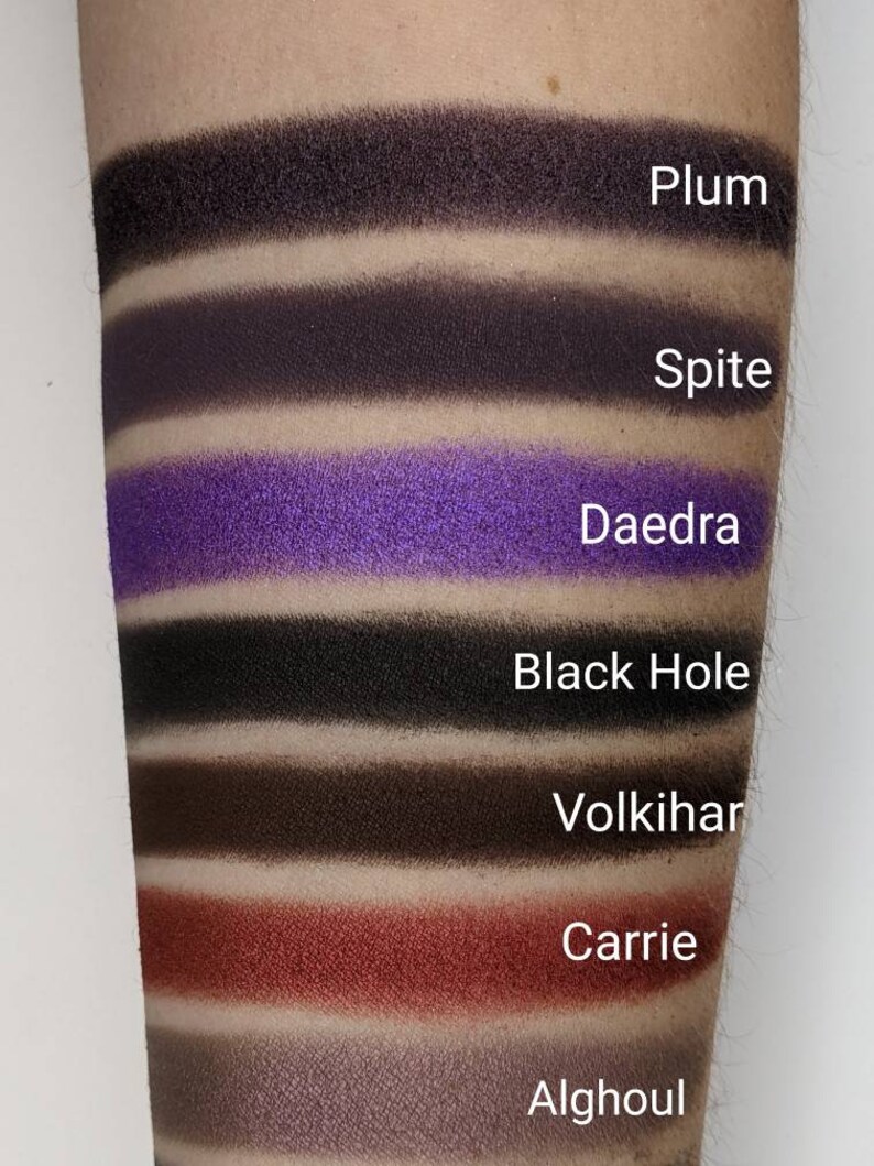Op de afbeelding: Een close-up van een make-up palet met zeven oogschaduw swatches. De swatches zijn van boven naar beneden gelabeld: Plum, Spite, Daedra, Black Hole, Volkihar, Carrie en Alghoul.