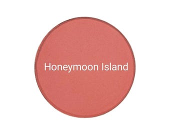 May include: A round, coral-colored blush compact with the text "Honeymoon Island" printed in white.