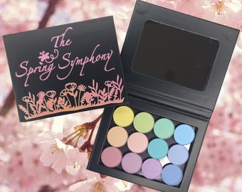 May include: A black eyeshadow palette with a mirror and the text "The Spring Symphony". The palette contains 10 round eyeshadows in pastel shades of pink, blue, green, and yellow.