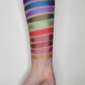 Puede incluir: Un primer plano de un brazo con muestras de sombra de ojos en varios colores, incluyendo azul, morado, verde, rojo, marr&oacute;n y dorado.
