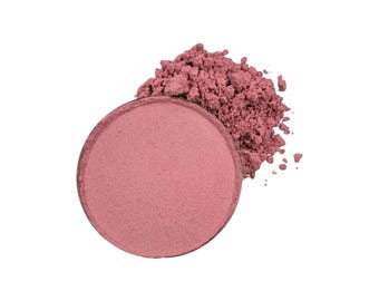 May include: A pink blush powder in a round container with some powder spilled out around it.