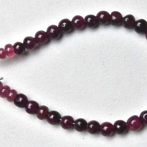 May include: A strand of pink and purple gemstone beads with silver clasps. The beads are graduated in size, with the larger beads at the center of the strand and the smaller beads at the ends.