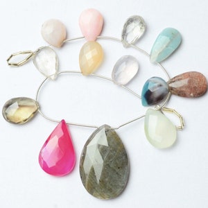 May include: A strand of gemstone beads, featuring a variety of colors and shapes, including pink, green, blue, brown, and clear. The beads are strung on a silver wire and are ready to be used for jewelry making.