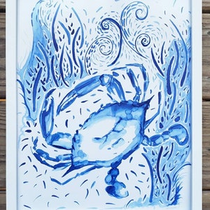 May include: Watercolor painting of a blue crab in a white frame. The crab is depicted in shades of blue, surrounded by stylized aquatic plants and swirling water elements. The artwork is framed in a simple white frame.