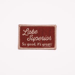 Puede incluir: Un parche rojo bordado con texto blanco que dice "Lake Superior" y "So good, it's great!"