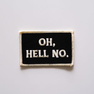 May include: A rectangular black patch with the embroidered words "OH, HELL NO." The text is in white, capital letters. The patch has a cream-colored border with a stitched design.