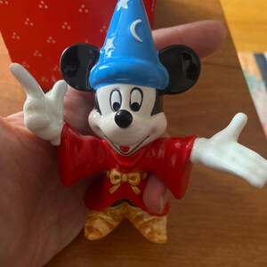 K&ouml;nnte beinhalten: Eine Keramikfigur von Mickey Mouse als Zauberer, mit einem blauen Hut mit Sternen und einem Halbmond. Er tr&auml;gt eine rote Robe und eine gelbe Hose. Die Figur hat schwarze Ohren und wei&szlig;e Handschuhe.