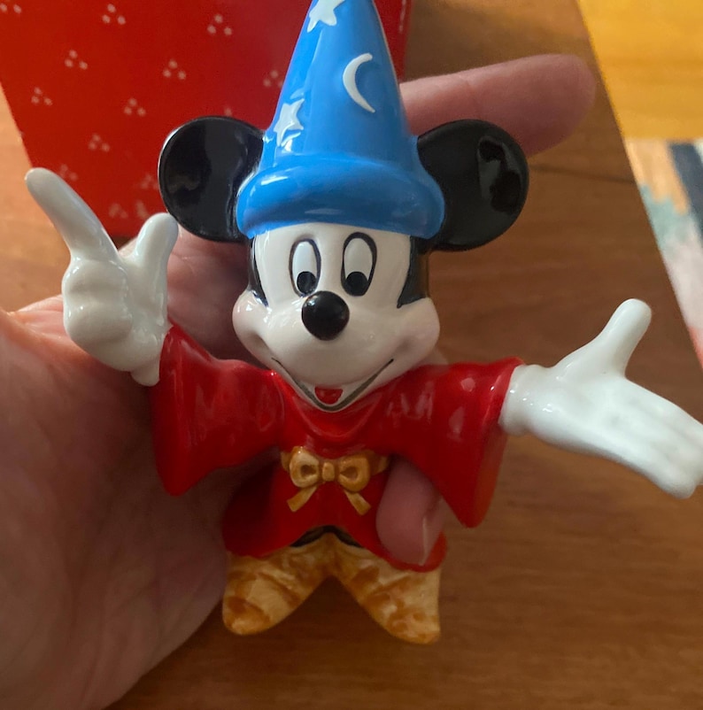 K&ouml;nnte beinhalten: Eine Keramikfigur von Mickey Mouse als Zauberer, mit einem blauen Hut mit Sternen und einem Halbmond. Er tr&auml;gt eine rote Robe und eine gelbe Hose. Die Figur hat schwarze Ohren und wei&szlig;e Handschuhe.