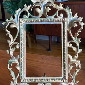 Peut inclure: Cadre photo de style vintage orné, de couleur or et vert. Le cadre présente des volutes complexes et une ouverture rectangulaire pour une photo. Le cadre a un petit support à l'arrière. Une pièce décorative pour la décoration intérieure.