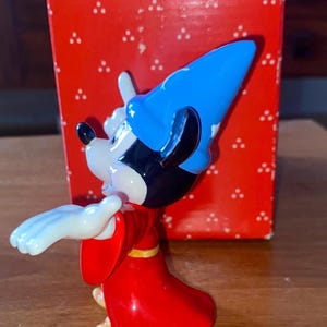 K&ouml;nnte beinhalten: Eine Mickey Mouse-Figur als Zauberer, mit blauem Hut und rotem Gewand. Die Figur steht vor einer roten Schachtel mit dem Wort "Sch". Ein Sammlerst&uuml;ck.
